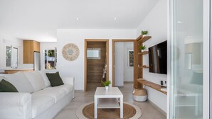 A modern living room with a white sofa, a coffee table, and a TV on a wooden shelf. - Casa Robert in Conil with Pool, Hot Tub, Garden, and Wi-Fi (Conil)