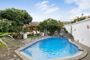 A swimming pool with a wooden deck, lounge chairs, and a pergola.