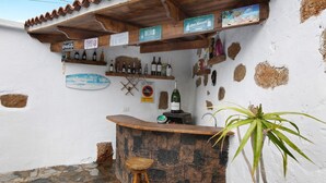 A bar area with a stone counter, wooden stools, and shelves with bottles. - Vacation Home "Casa Candelaria" with Views of El Teide, Private Pool & Wi-Fi (Arico)