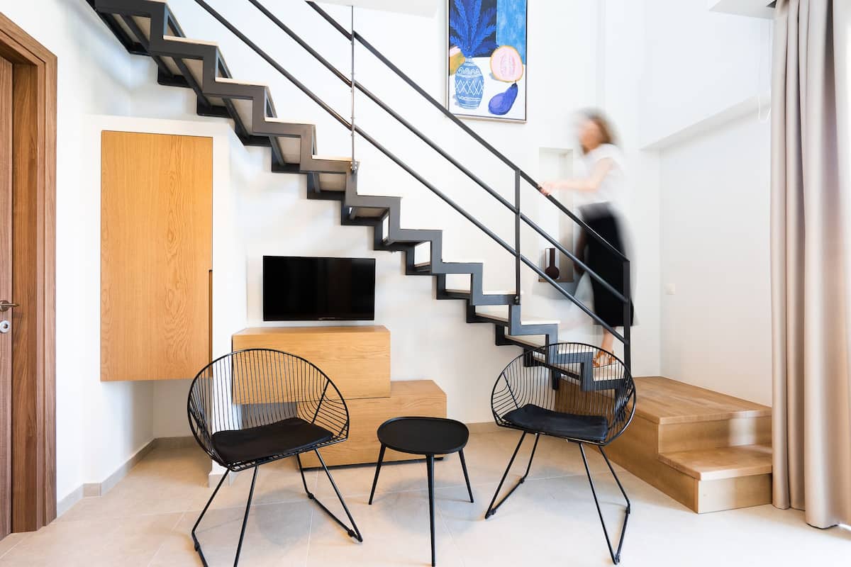 A modern interior with a staircase, black chairs, a wooden cabinet, and a flat-screen TV.