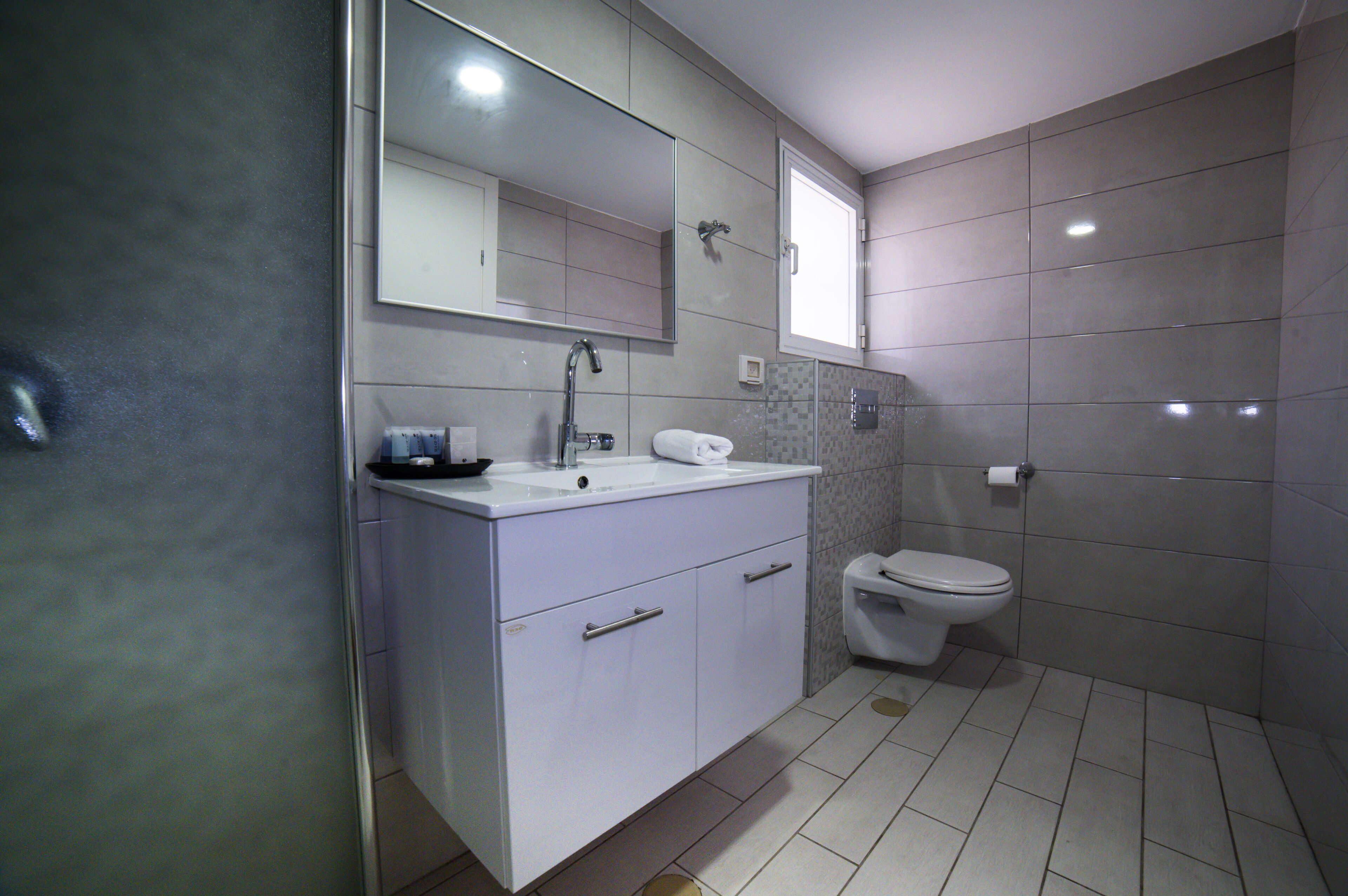 Un bagno moderno con un mobile lavabo bianco, uno specchio grande, un WC e pareti piastrellate.