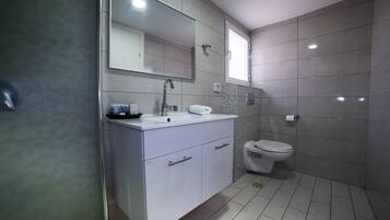 Un bagno moderno con un mobile lavabo bianco, uno specchio grande, un WC e pareti piastrellate.
