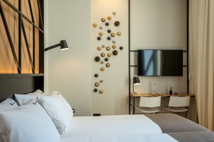 Hotellihuone, jossa on sänky, työpöytä ja kaksi tuolia, televisio sekä seinään kiinnitetty valaisin.
