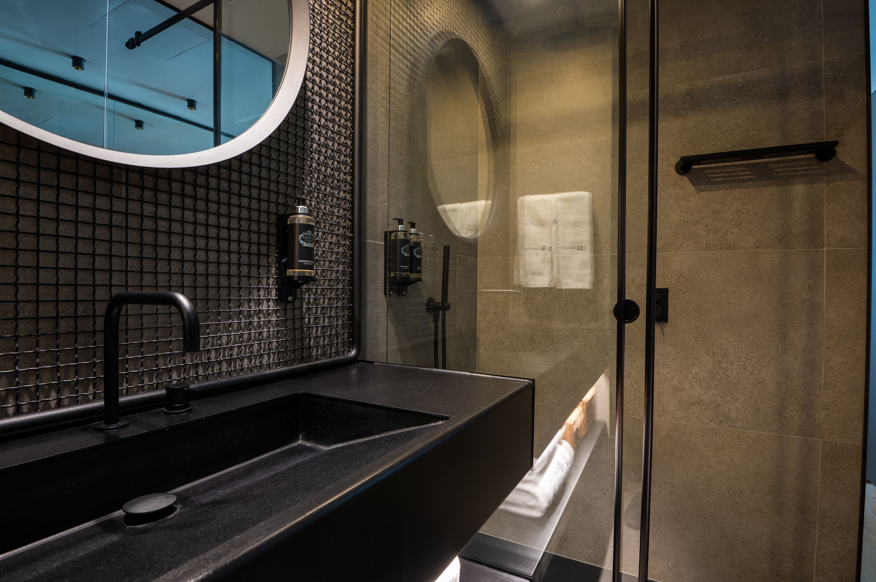 Ein modernes Badezimmer mit einem schwarzen Waschbecken, einem großen Spiegel und einer gläsernen Dusche.
