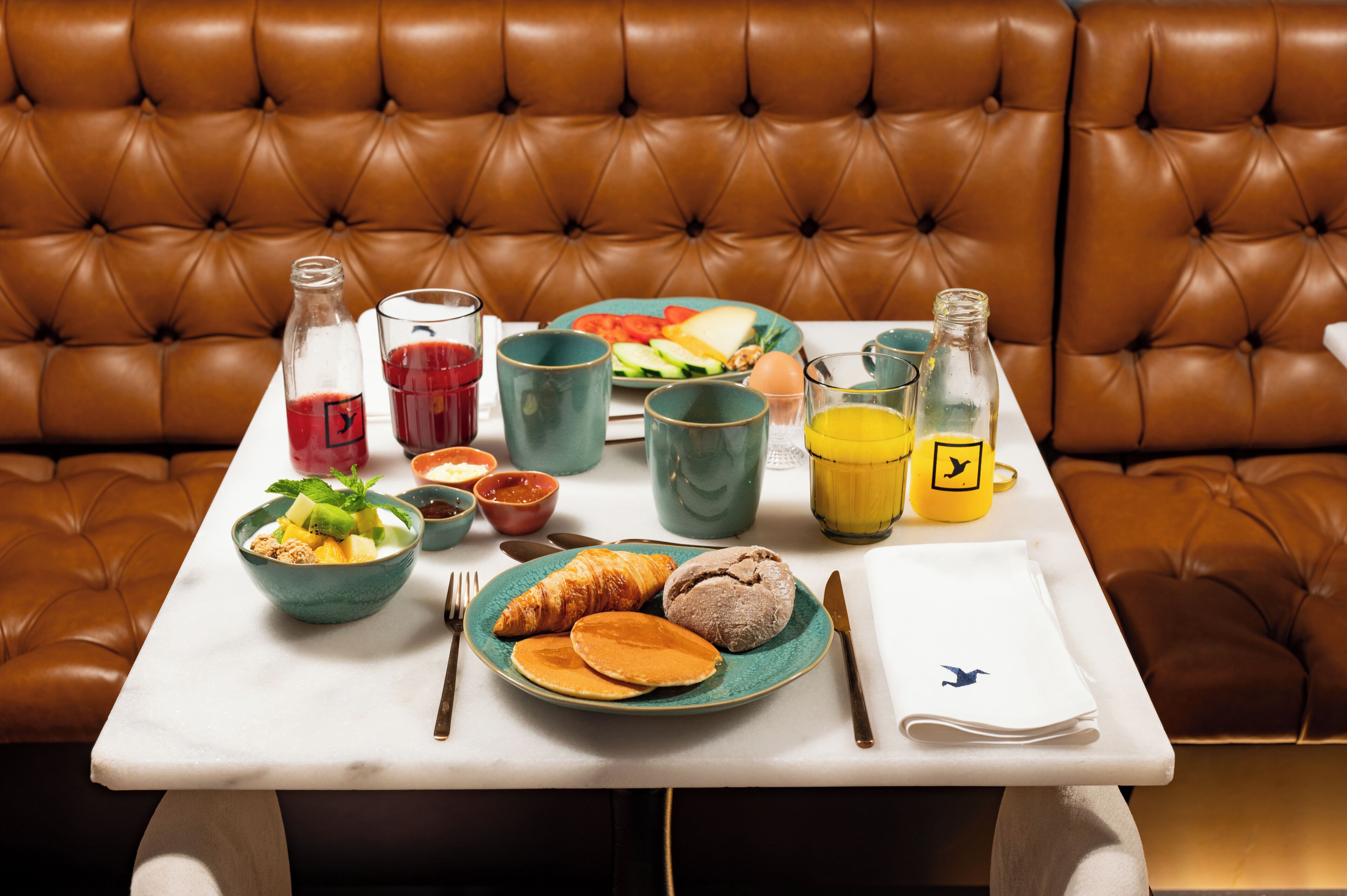 Un desayuno con una mesa, comida, bebidas y un sofá de cuero marrón al fondo.
