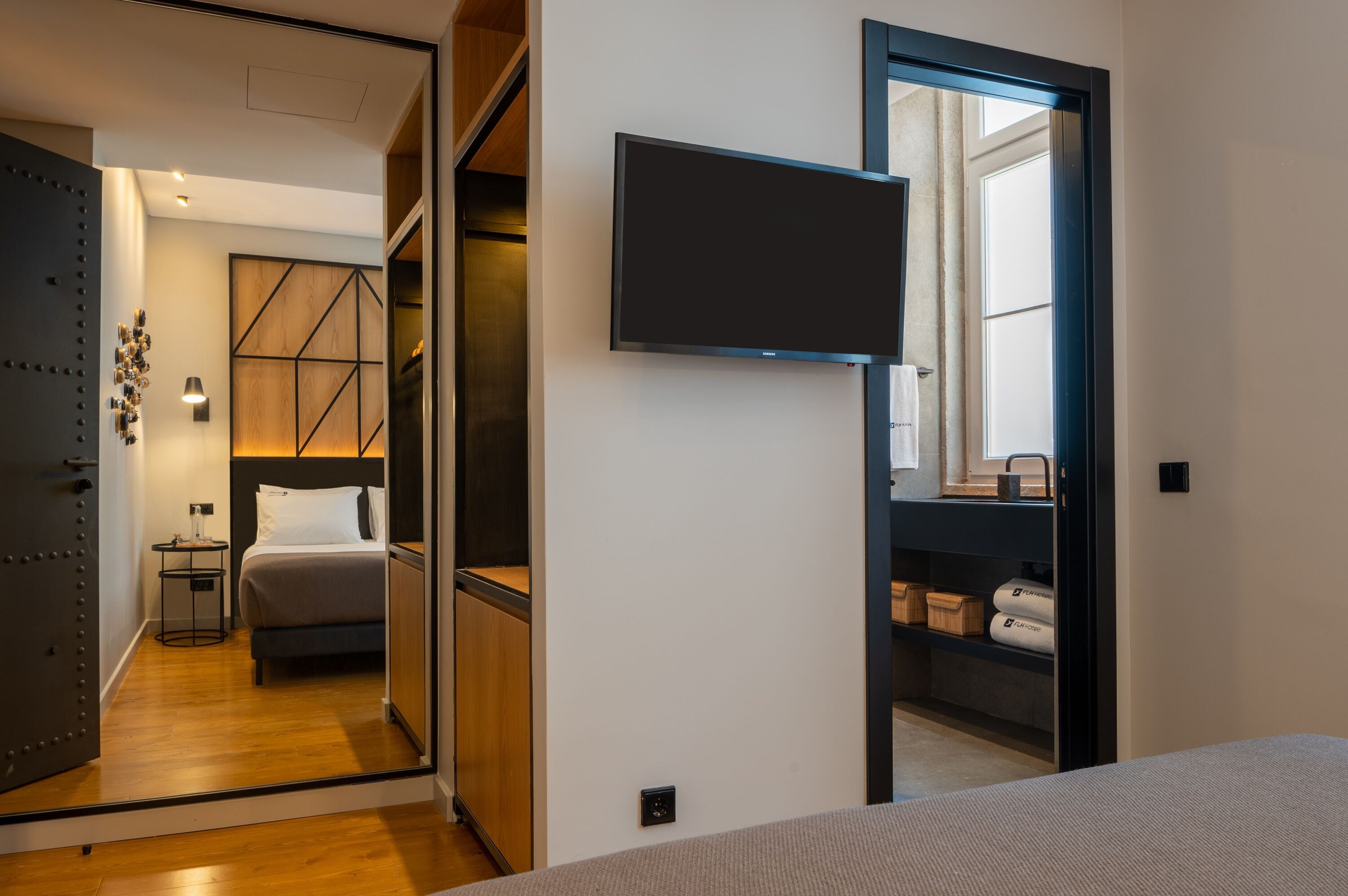 A modern hotel room with a bed, bedside table, and a flat-screen TV mounted on the wall.