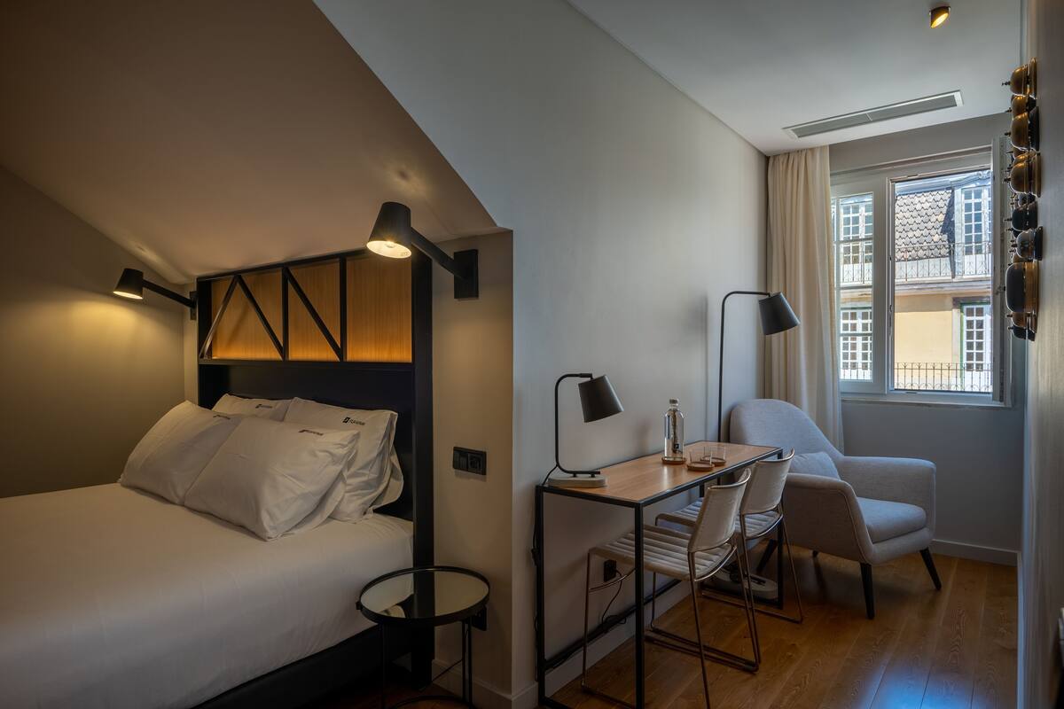 Una habitación de hotel moderna con cama, escritorio, silla y vistas a la ciudad desde la ventana.