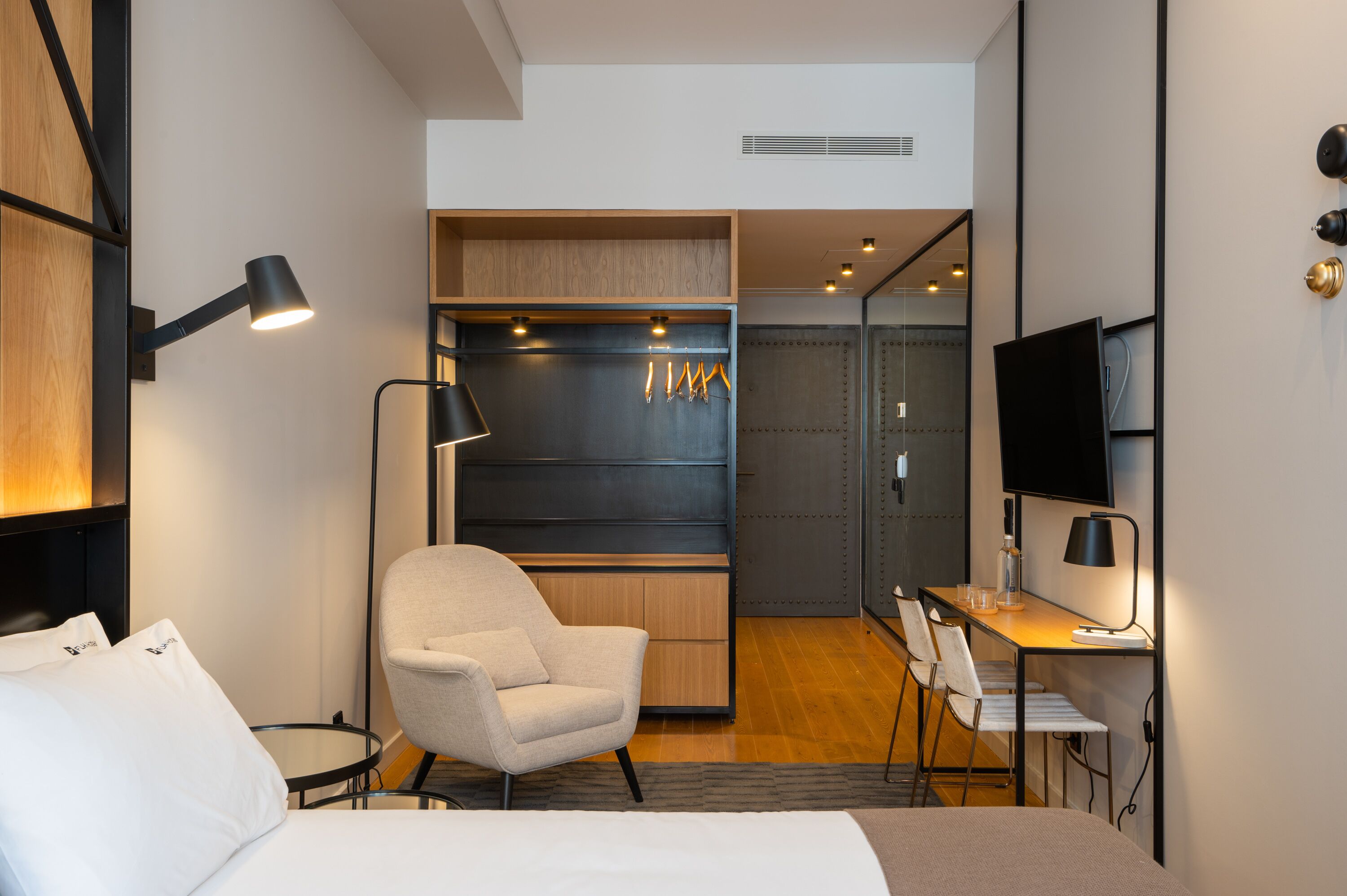 A modern hotel room with a bed, a desk, a chair, a TV, and a wardrobe.