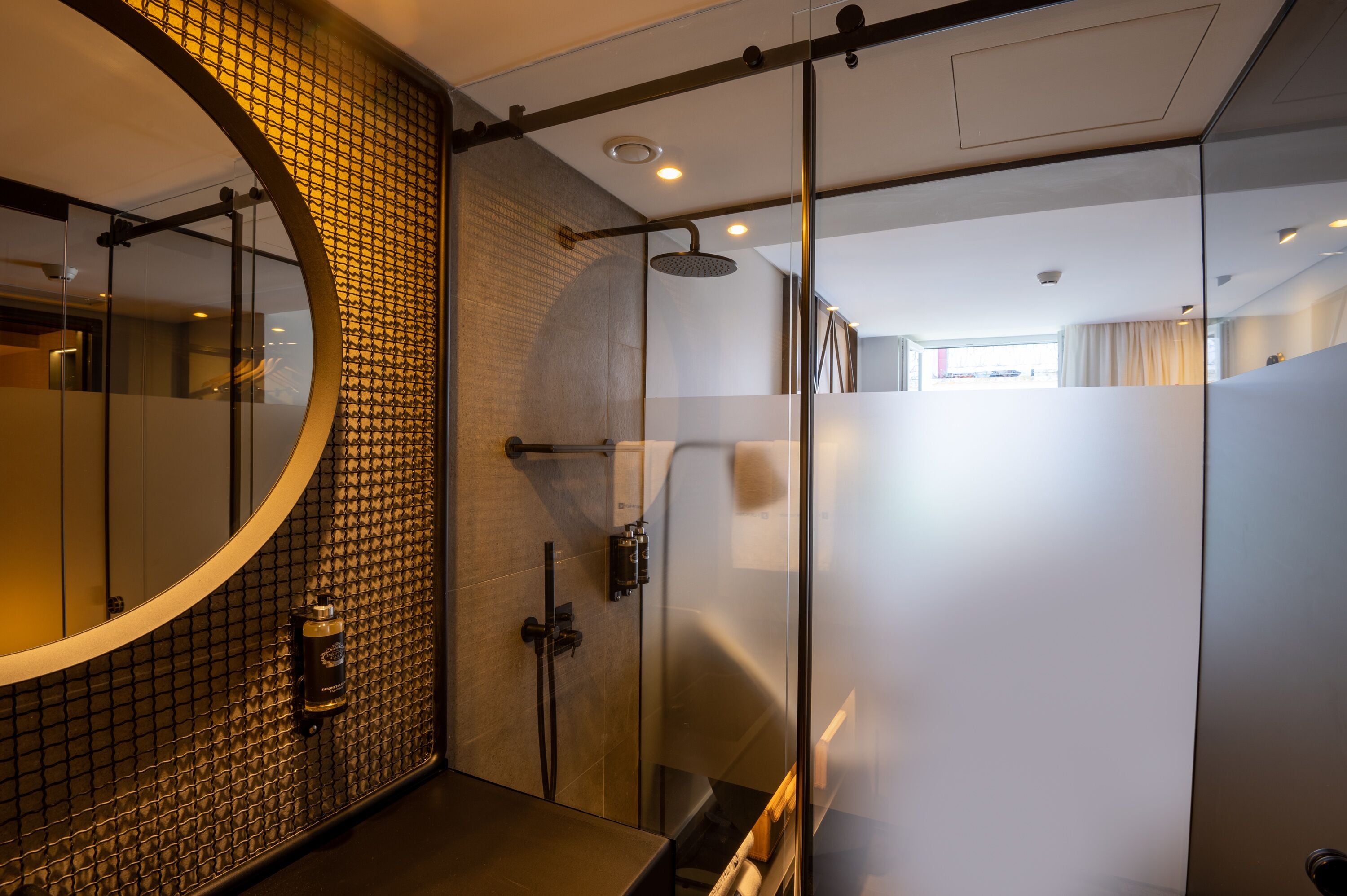A modern bathroom with a glass shower enclosure, a round mirror, and a tiled wall.