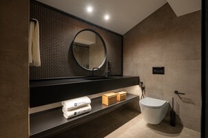 A modern bathroom with a large mirror, a toilet, and a shelf with towels and toiletries.