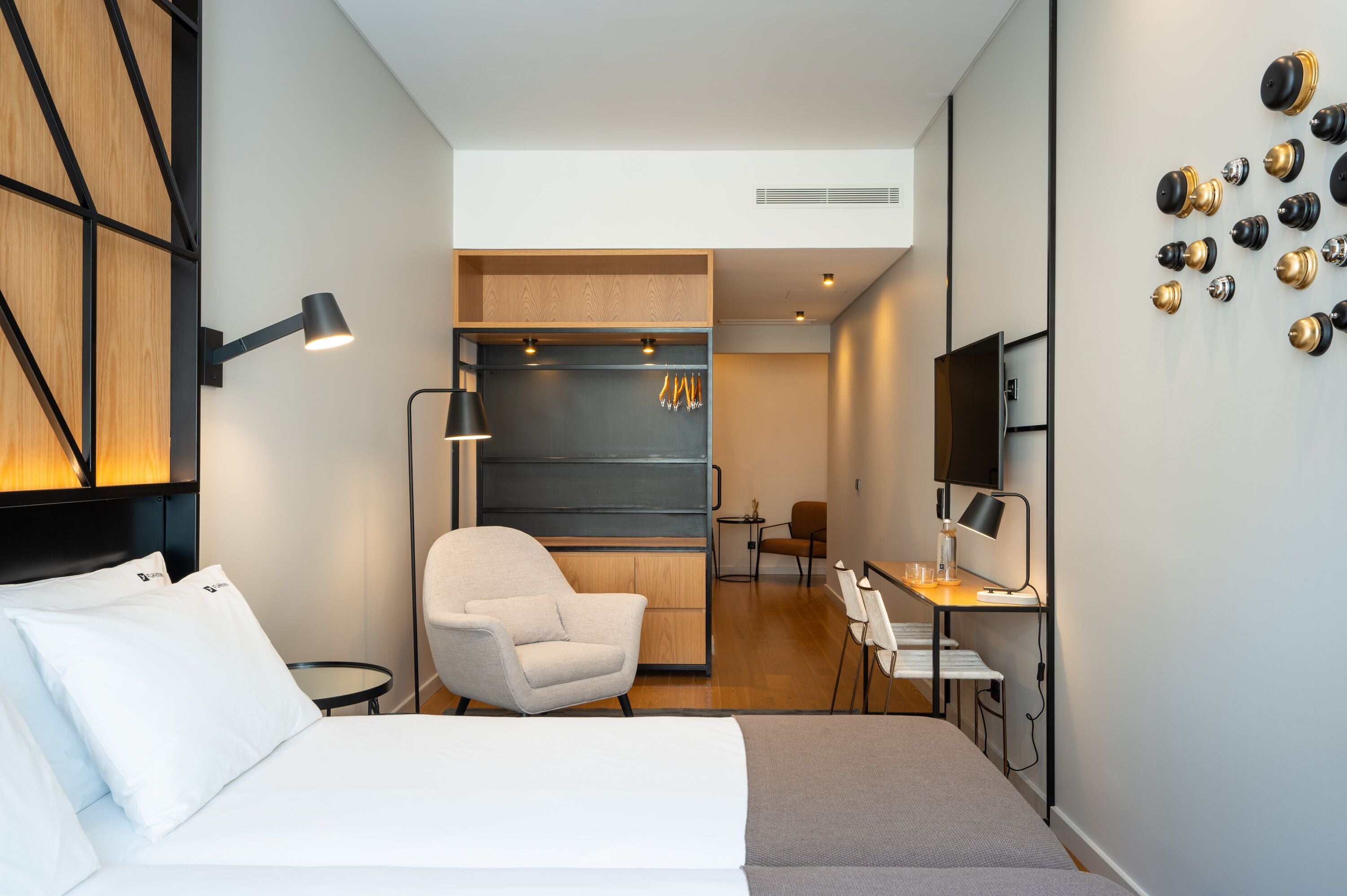 Quarto de hotel moderno com cama, escrivaninha, cadeira e televisão.