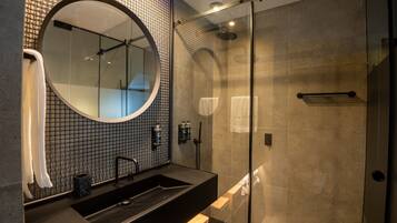Un baño moderno con un espejo redondo grande, un lavamanos negro y una zona de ducha con mampara de cristal.