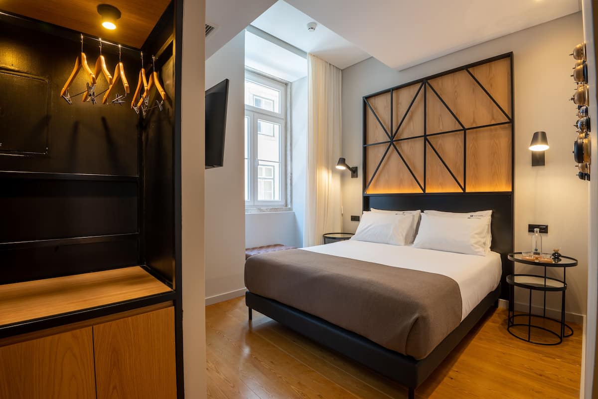 Habitación de hotel moderna con una cama grande, cabecera de madera, televisor montado en la pared y una mesita de noche.