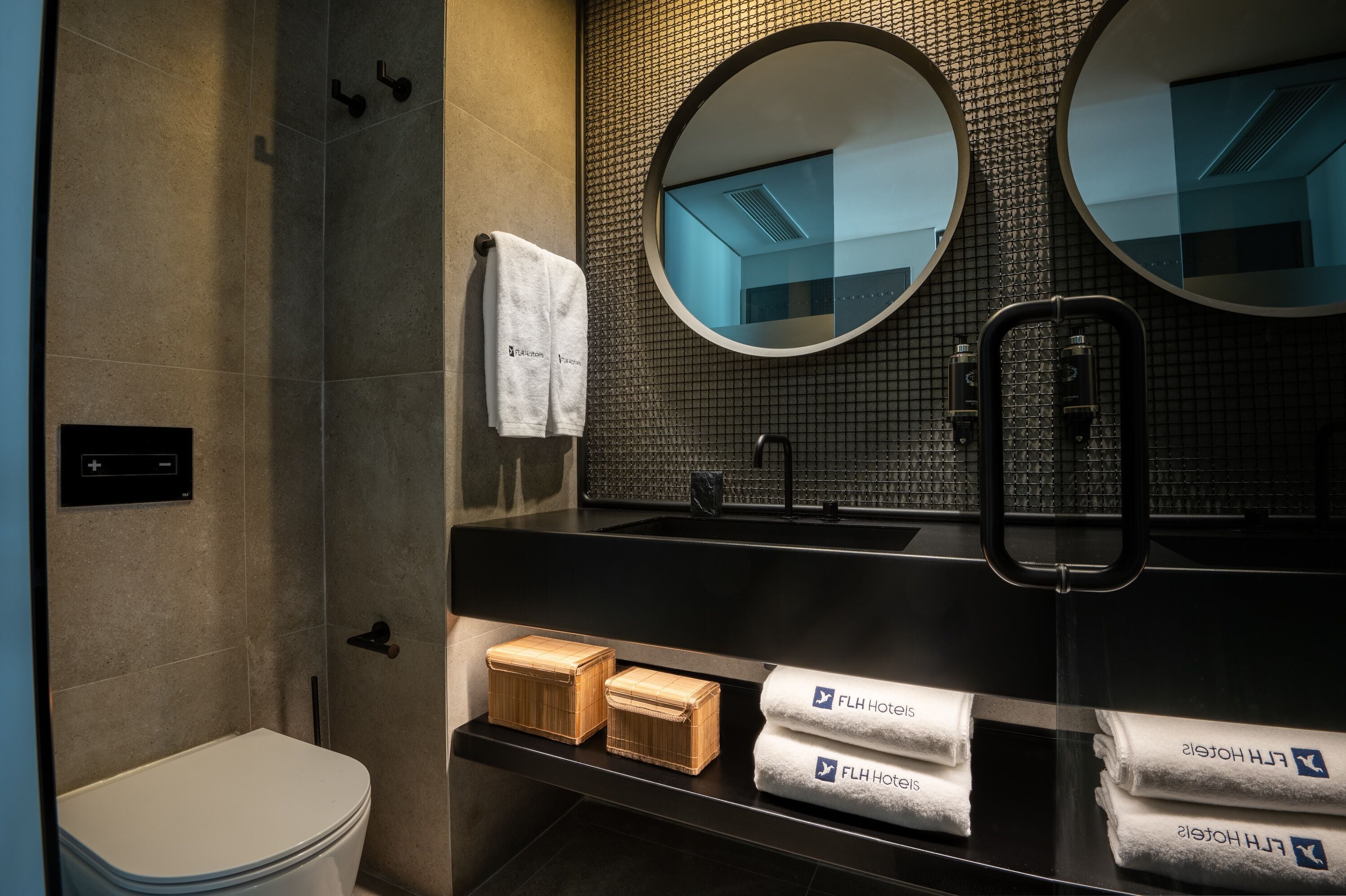 A modern bathroom with a toilet, two round mirrors, a black sink, and a towel rack.