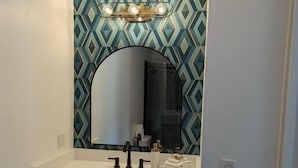 Ein Badezimmer mit weißem Waschtisch, einem großen Spiegel und einer Rückwand mit geometrischem Muster.