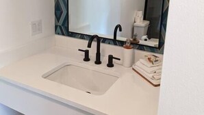 Ein Badezimmer mit einem weißen Waschbecken, schwarzen Wasserhähnen und einem großen Spiegel.