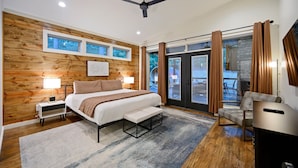 Ein modernes Schlafzimmer mit einer Holzwand, einem großen Bett, einer Bank, einem Fernseher und einem Balkon mit Vorhängen.