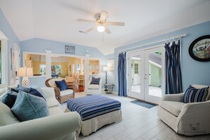 A spacious room with a bed, two sofas, a ceiling fan, and a view through a glass door.