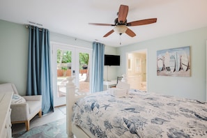 A bedroom with a bed, a ceiling fan, a TV, a desk, and a painting of surfboards.