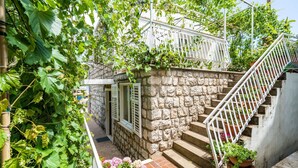 Un escalier en pierre avec des rampes blanches, menant à un balcon blanc orné de plantes en pot.
