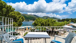 Une terrasse avec des chaises blanches et une table donnant sur une étendue d’eau, avec des montagnes en arrière-plan.