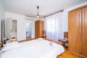 A bedroom with a bed, a wooden wardrobe, a chair, and a desk with a lamp. - Apartments Zarac (Dubrovnik)