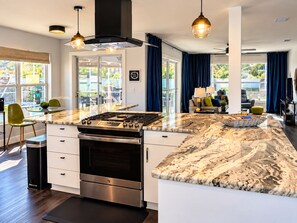 A modern kitchen with a large island, stainless steel appliances, and a view to the outdoor seating area. - The Coconut Courtayrd-Private Pool& Tiki Hot Tub-Minutes From Fun-Walk 2 Golf (The Villages)