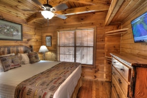 A wooden cabin bedroom with a bed, a dresser, a ceiling fan, and a window with blinds.