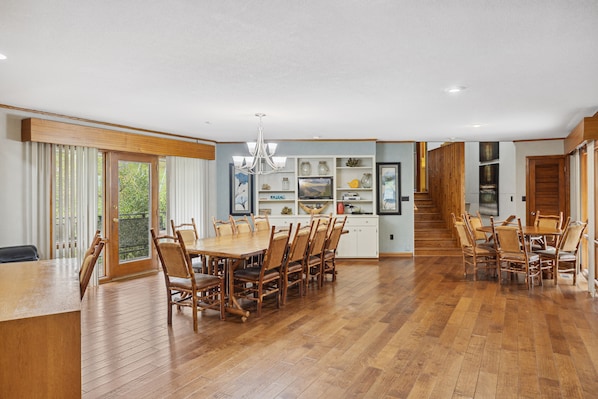 A spacious dining area with wooden flooring and a central island, flanked by wooden chairs and a large table.