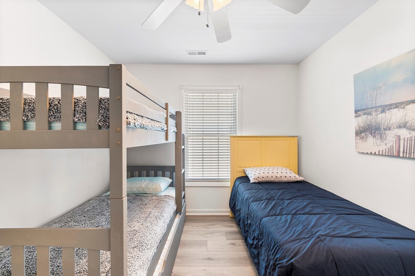 A room with bunk beds, a window with blinds, a ceiling fan, and a painting on the wall.