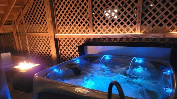 Een hottub met blauwe verlichting, omgeven door houten lattenwanden en een houten dak.