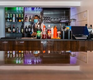 A bar area with a bartender, shelves of various liquor bottles, and a digital payment terminal. - Isglo Hotels Ikoyi (Lagos)