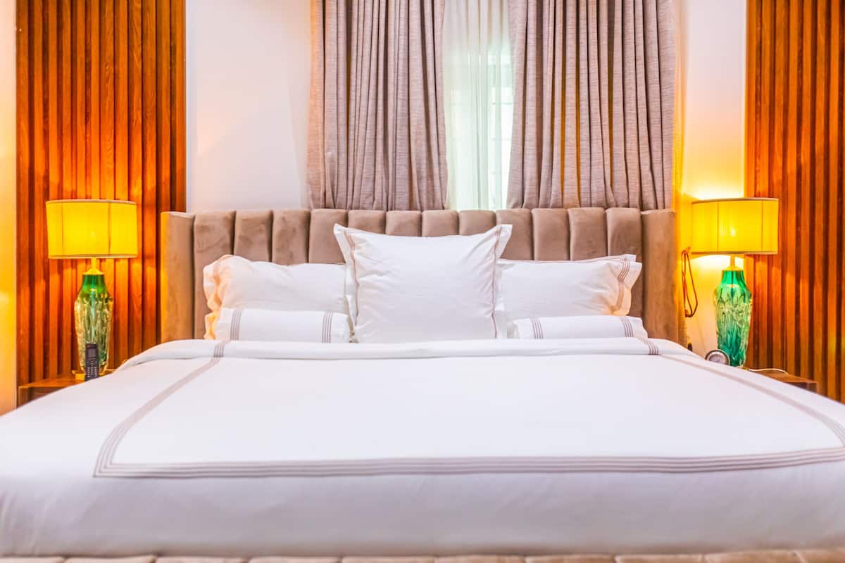 A large bed with white linens, two bedside lamps, and a wooden headboard.