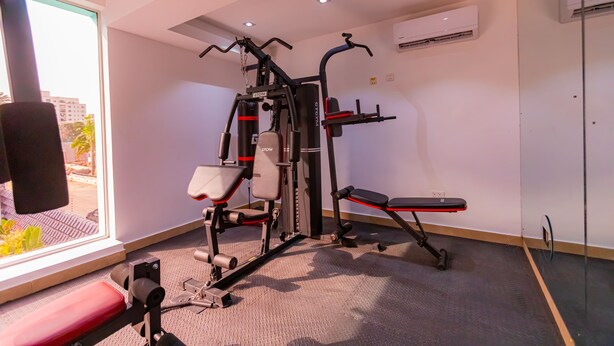 Een sportschool met trainingsapparatuur, een bank en een raam met uitzicht op gebouwen en bomen.