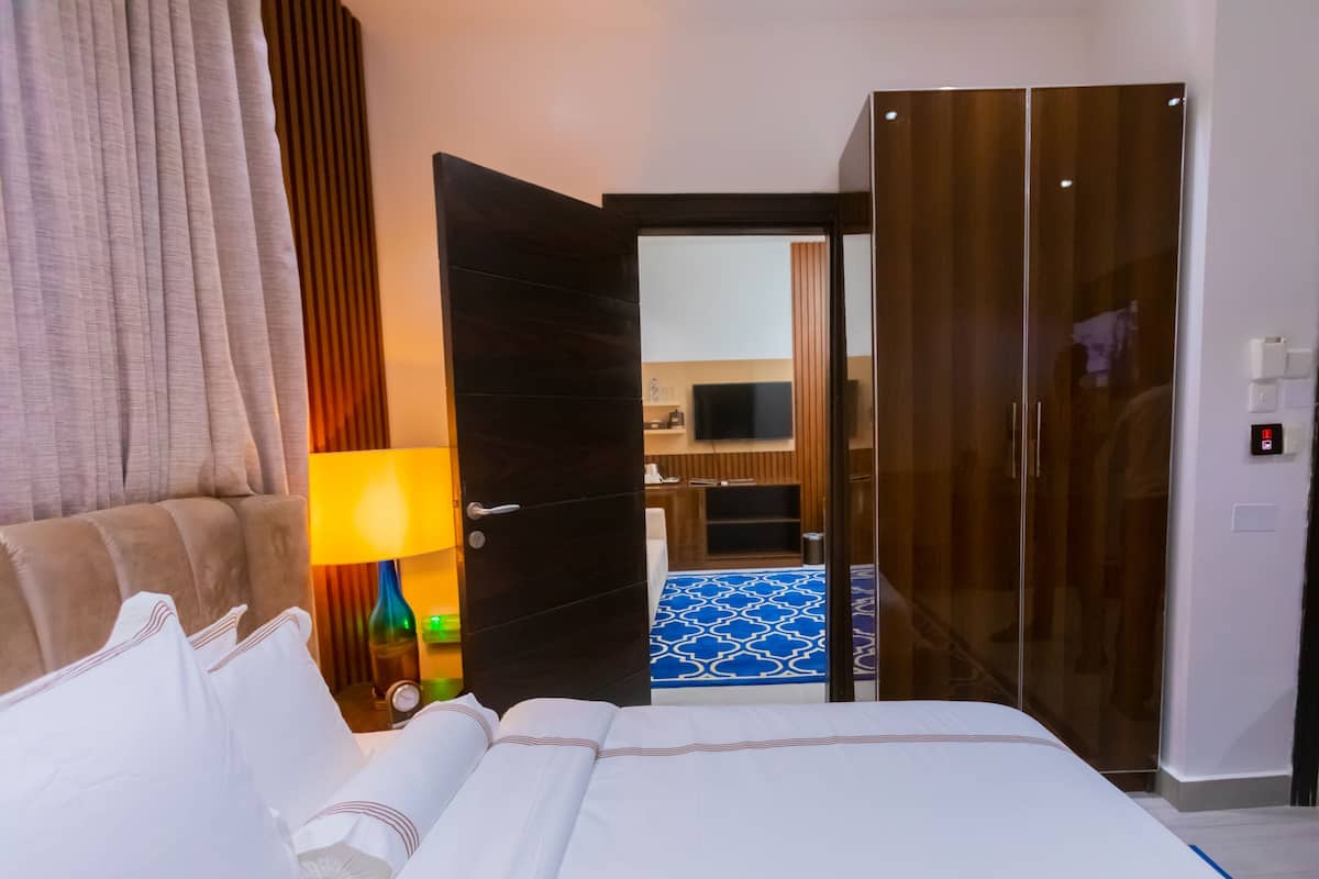 A hotel room with a bed, a lamp, a wardrobe, and a television in the background.