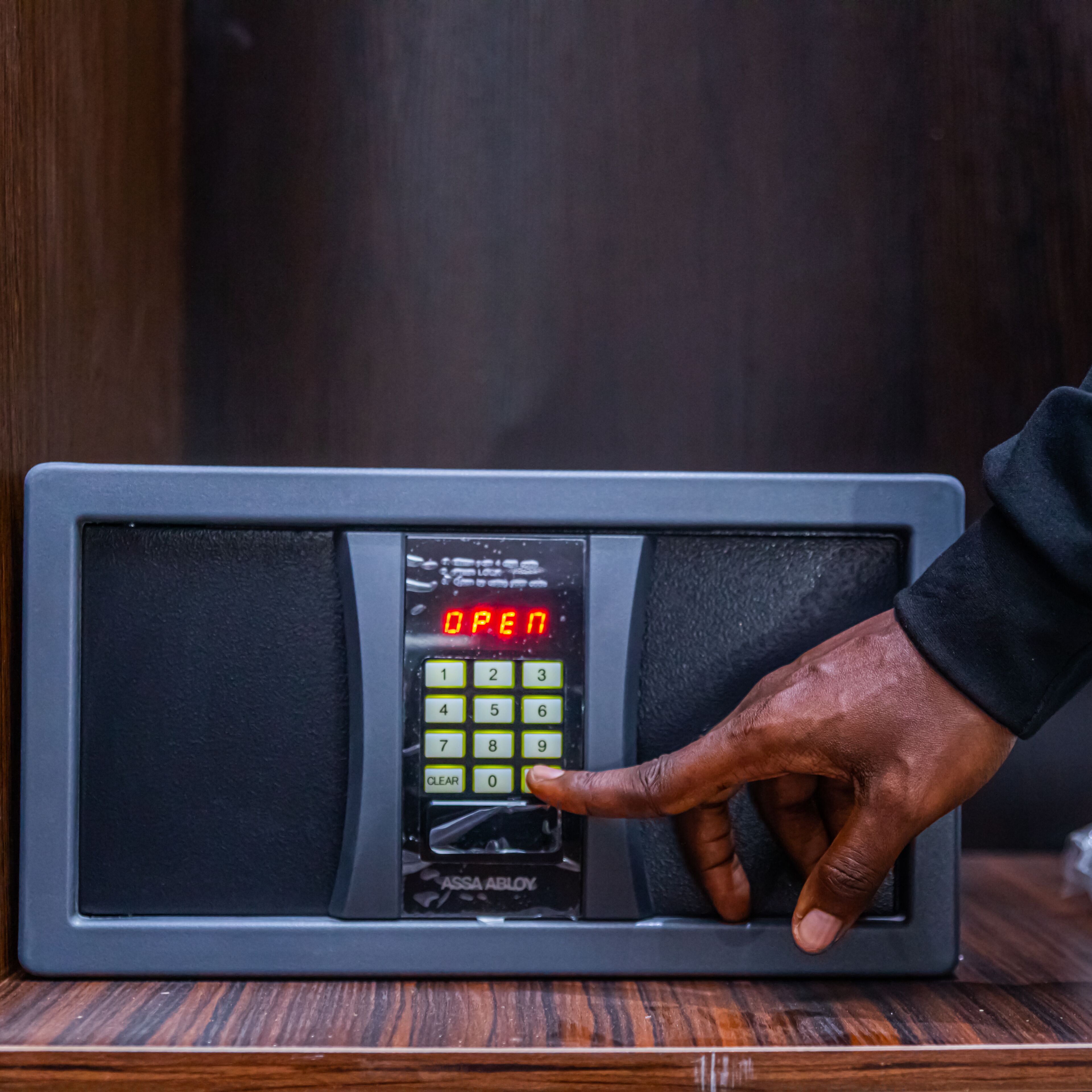 A keypad with a digital display reading "OPEN" and a hand pressing the number 0 key.