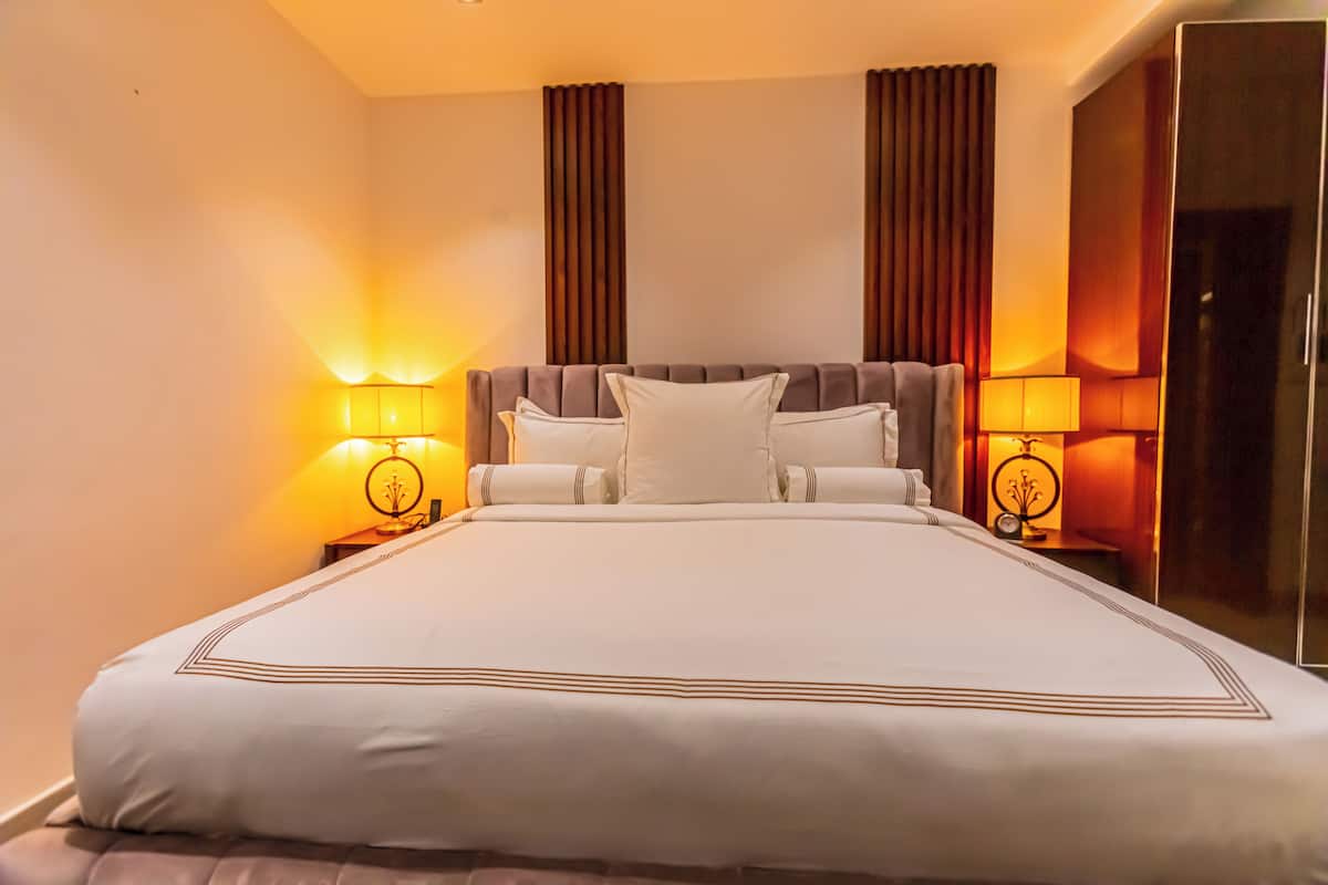 A neatly made bed with a white and brown color scheme, flanked by two bedside lamps with a classic design.