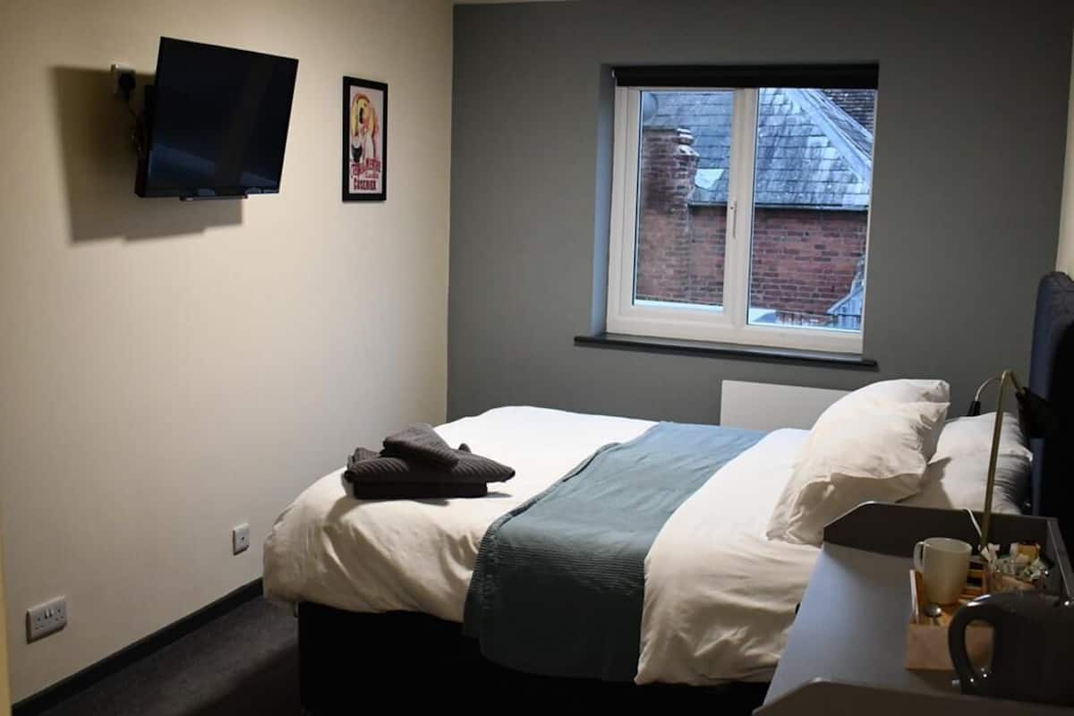 A bedroom with a bed, a desk, a window, and a mounted TV.