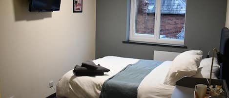 A bedroom with a bed, a desk, a window, and a mounted TV.