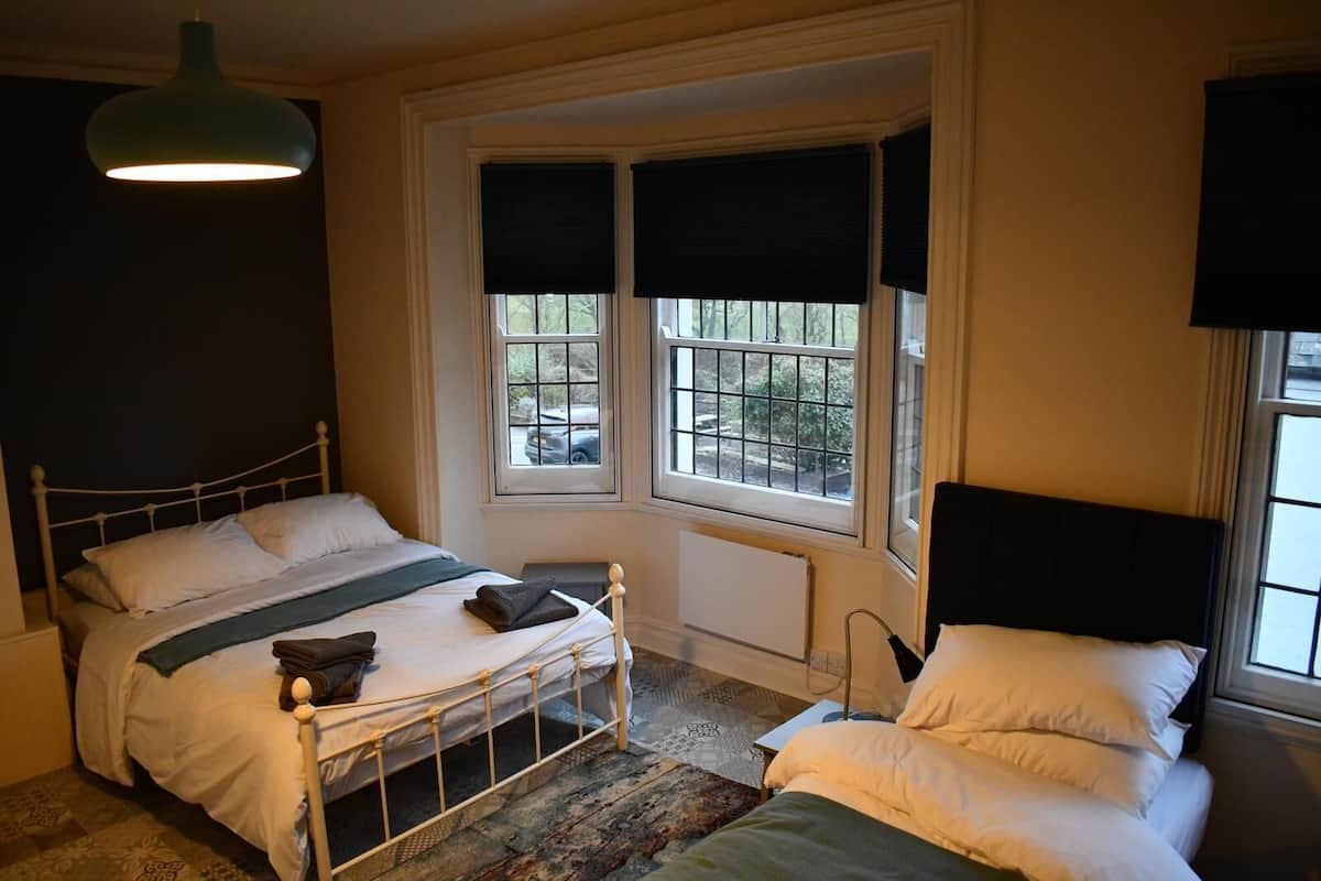 A bedroom with a single bed, a window with blinds, a radiator, and a hanging light fixture.