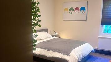 Un dormitorio con una cama, una mesita de noche, una lámpara, una ventana con persianas y un cuadro en la pared.
