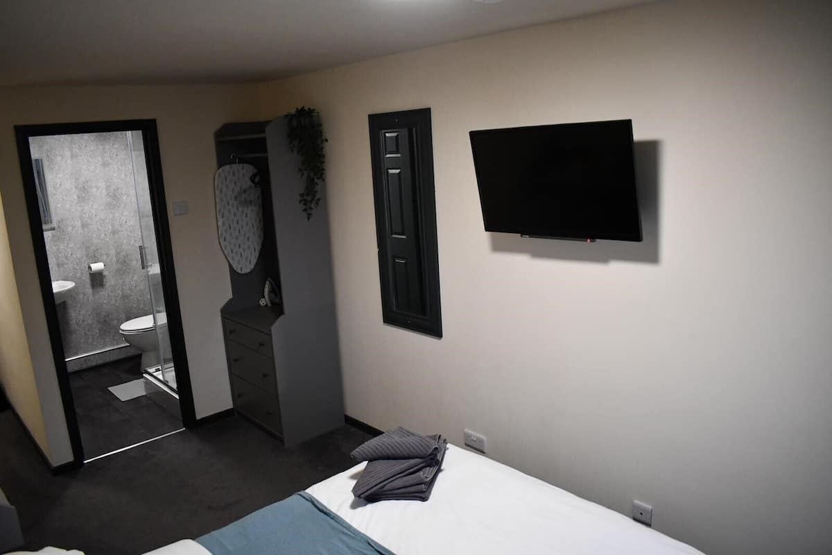 A hotel room with a bed, a TV mounted on the wall, a bathroom with a toilet and sink, and a door leading to another room.