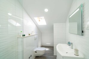 A modern bathroom with a skylight, white tiles, a white toilet, a white sink, and a mirror.