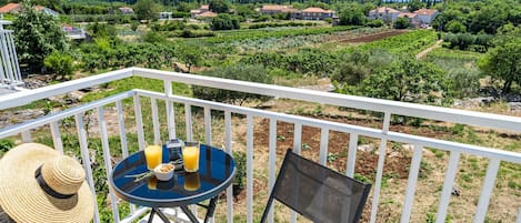 A balcony with a table, chairs, and a view of vineyards and houses.