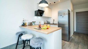 A modern kitchen with a central island, bar stools, a stainless steel refrigerator, and a pendant light. - Apartments Amalija (Konavle)