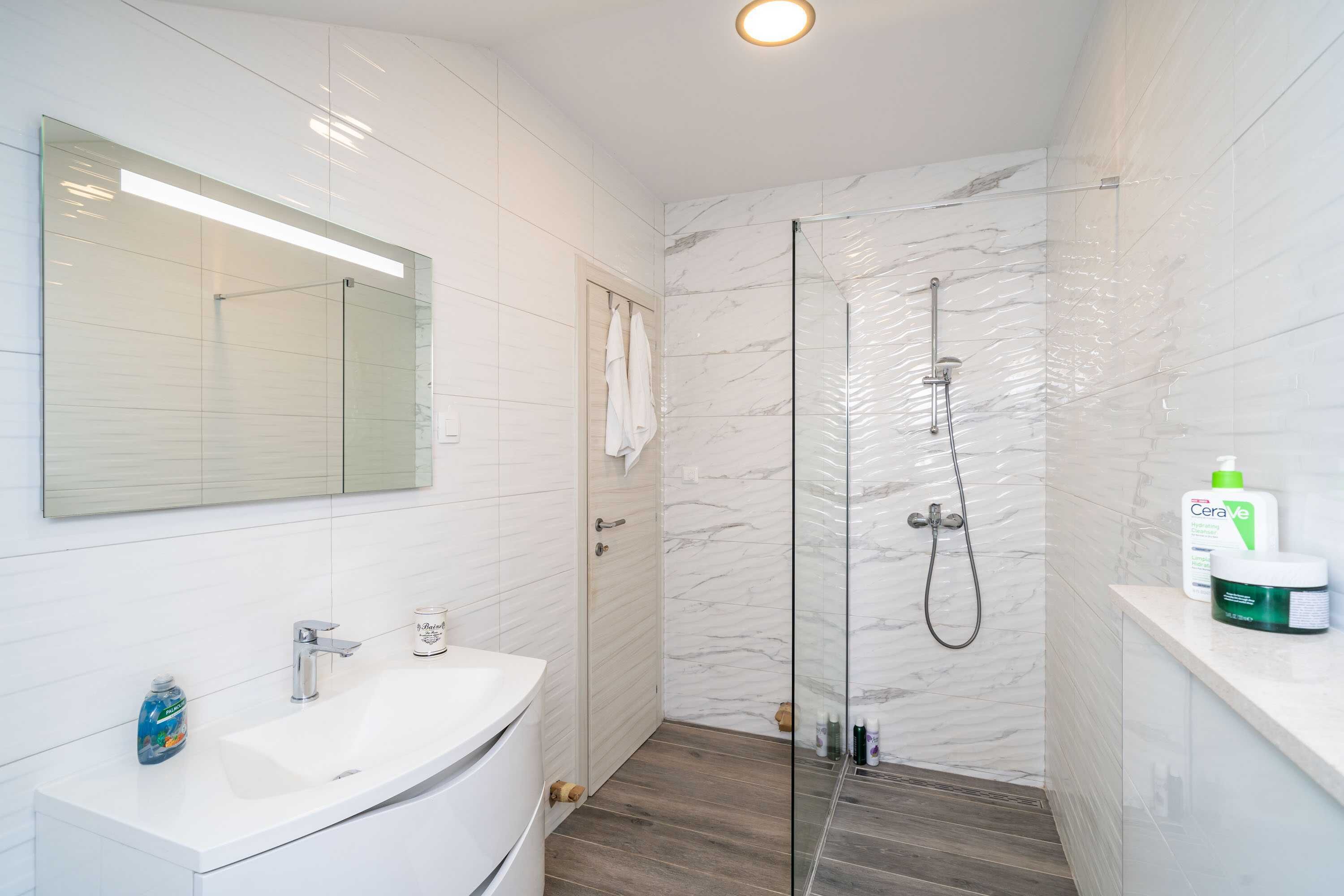 Ein modernes Badezimmer mit einer in Glas eingefassten Dusche, einem weißen Waschbecken und einem Spiegel darüber.
