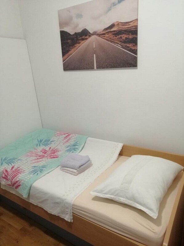 A single bed with a floral bedspread, a folded towel, and a white pillow. - Apartment Spalato (Bibinje)