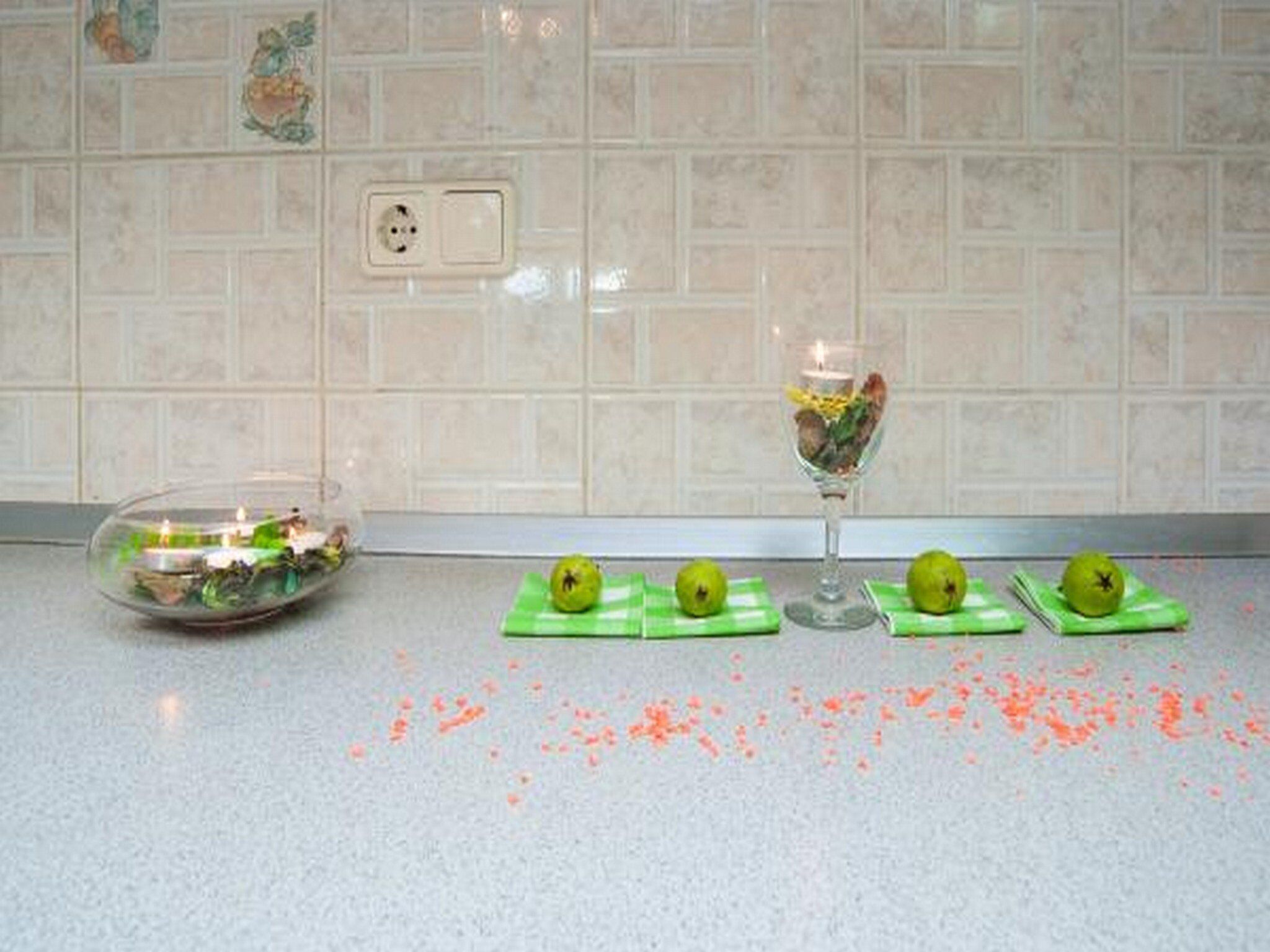 A kitchen with a tiled backsplash, a power outlet, and a glass bowl with a candle on the counter.