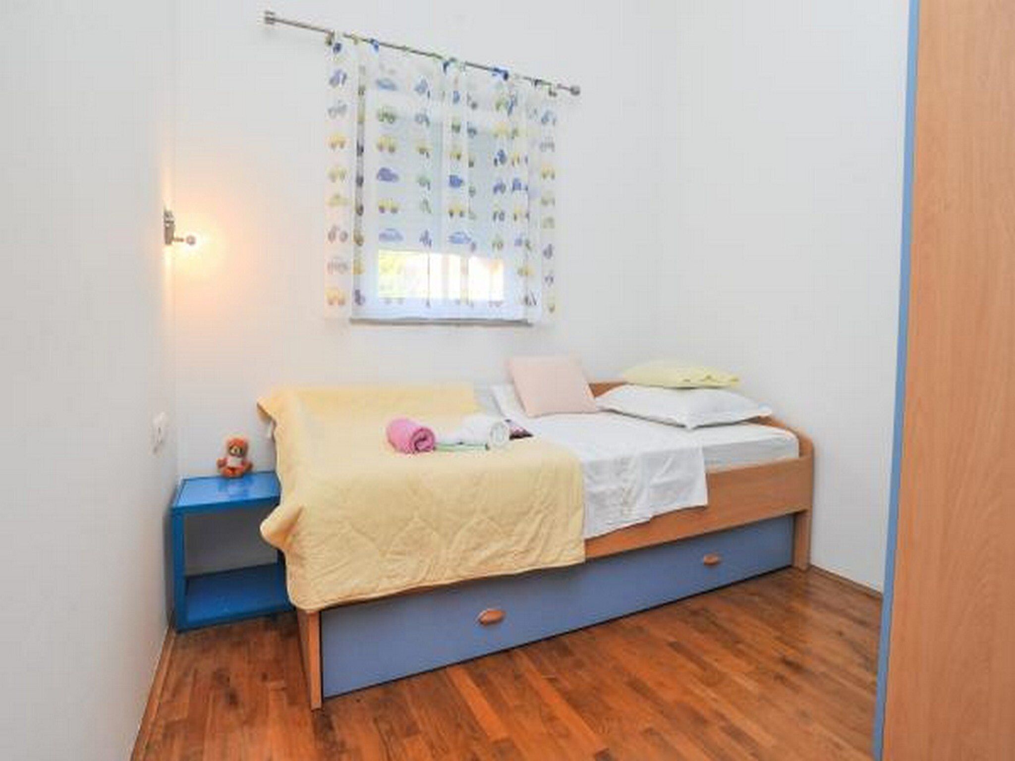 Ein Schlafzimmer mit einem Bett, einem Nachttisch, einem Fenster mit Vorhängen und Holzboden.