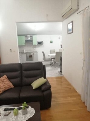 A living room with a dark sofa, a coffee table with decorative items, and a view into a kitchen and dining area with a white table and chairs.